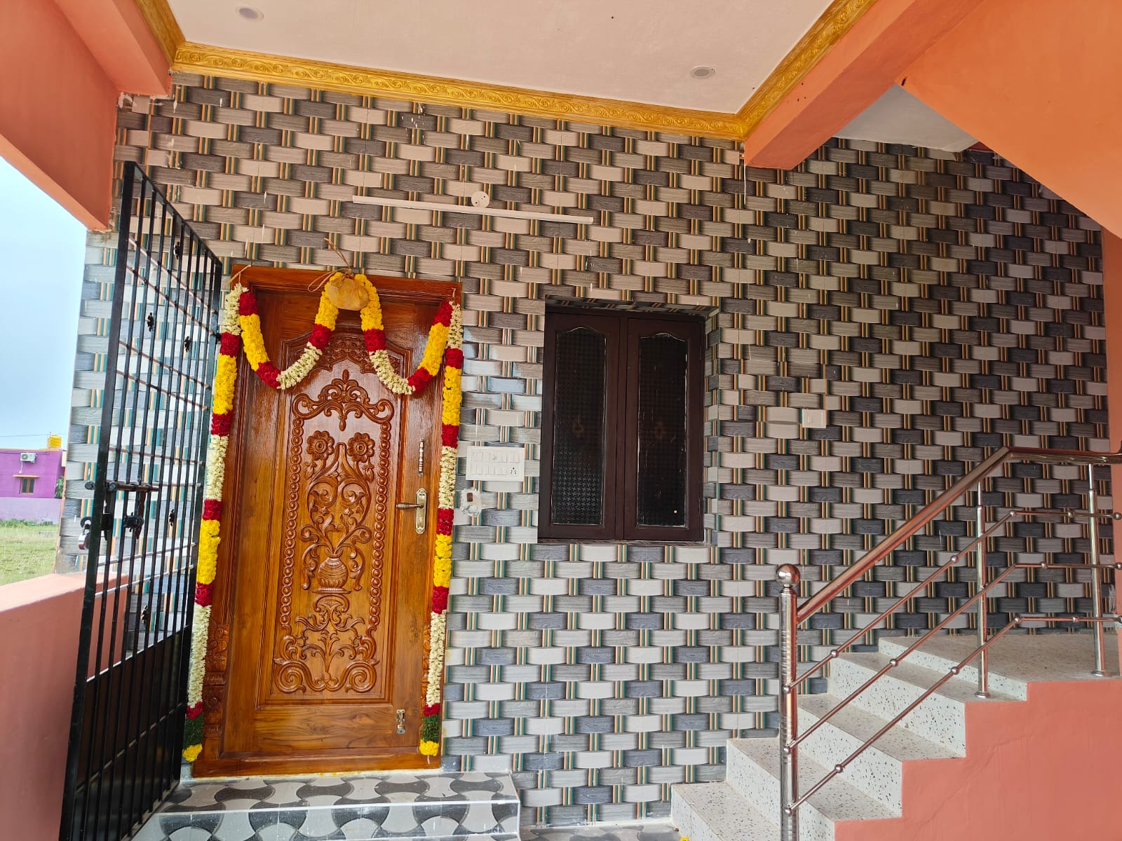 Finished entrance foyer with a carved wooden door, marigold garland and decorative tile wall, VK Builders interior work