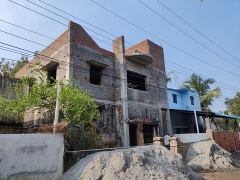Exposed red-brick two-storey house mid-construction with sand piles in the yard, VK Builders site