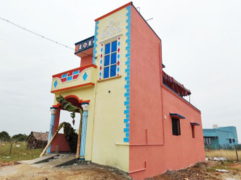 Completed yellow and coral house with banana-leaf entrance arch, VK Builders project