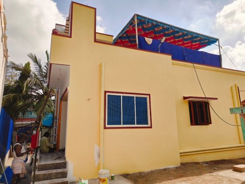 Yellow house with maroon-trimmed gable peak, workers touching up exterior paintwork, VK Builders painting work