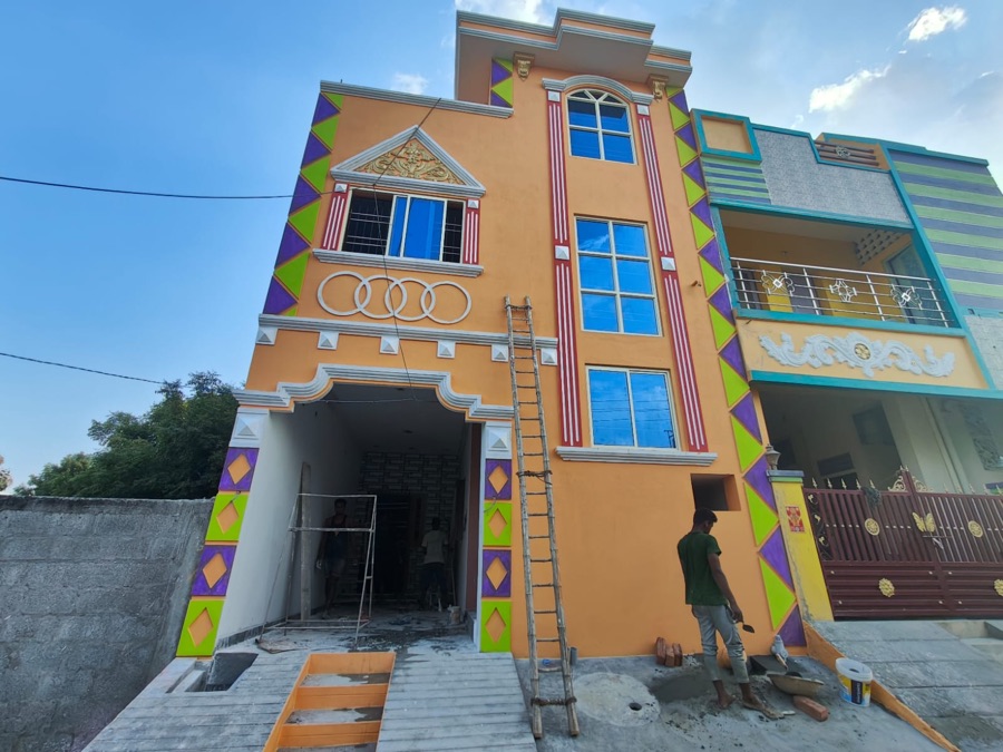 The same VK Builders house at the painting stage, orange facade with red and green diamond trim being finished